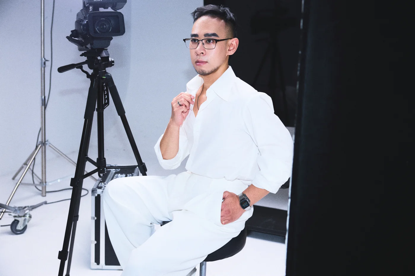 Kane Diep seated beside a camera in a white suit and glasses