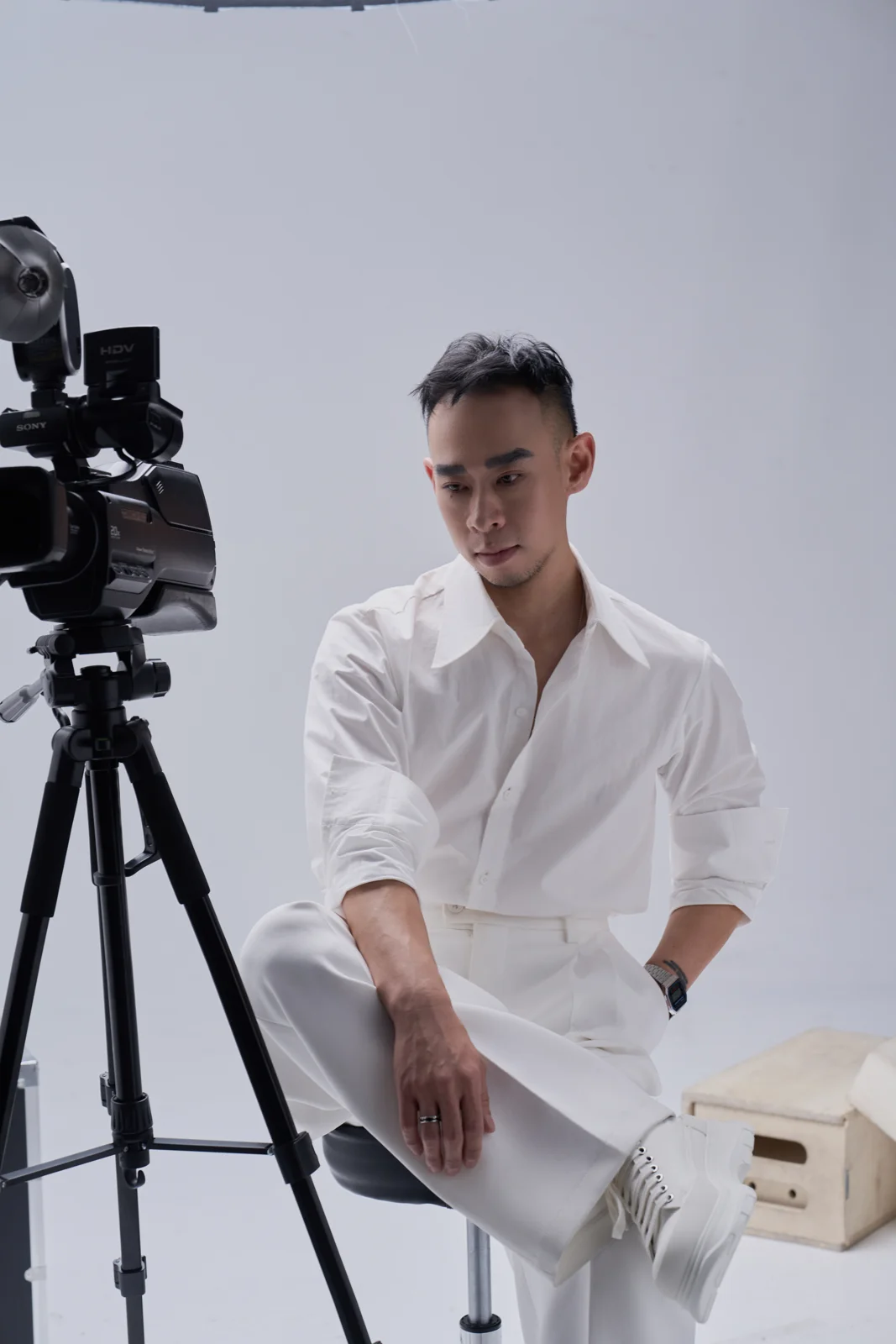 Kane in a white outfit seated beside a film camera